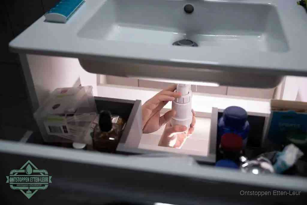 Een pompfles met zeep boven een wastafel, de heet water en afwasmiddel-methode om een vetprop in de afvoer los te maken in Etten-Leur