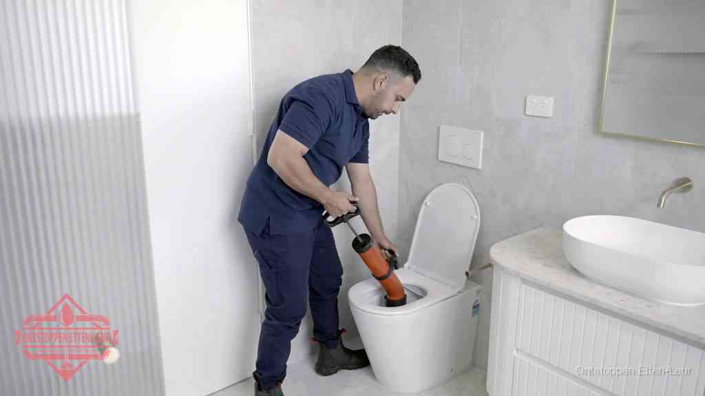 Een monteur buigt over een wandcloset en duwt met de hand een persluchtontstopper in de toiletpot om de verstopping handmatig los te maken in Etten-Leur