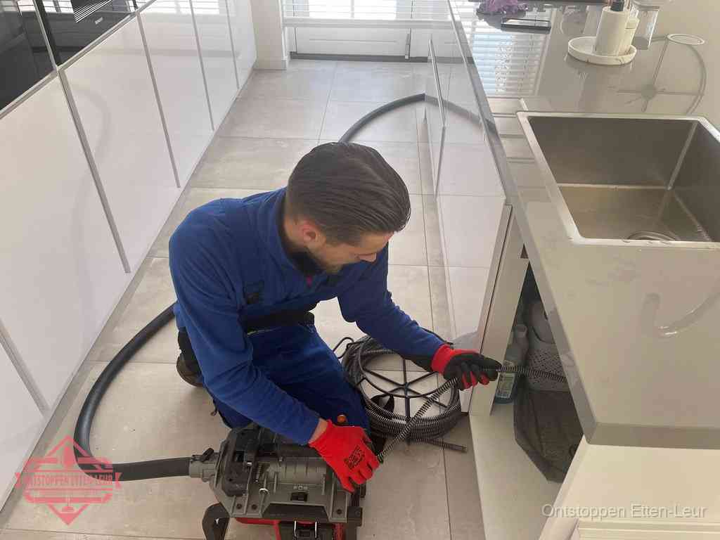 Een monteur ontstopt de keukenafvoer onder de spoelbak met een elektrische veermachine in Etten-Leur