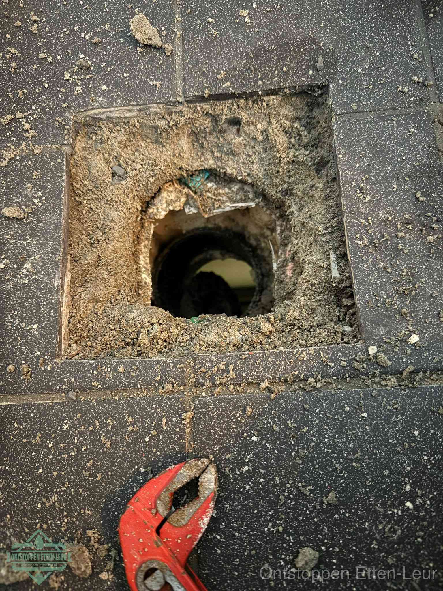 Een geopend rioolputje in een betontegelvloer met losgemaakt rooster en een zichtbare ronde afvoerbuis, het achterhalen waar de afvoerverstopping zit in Etten-Leur