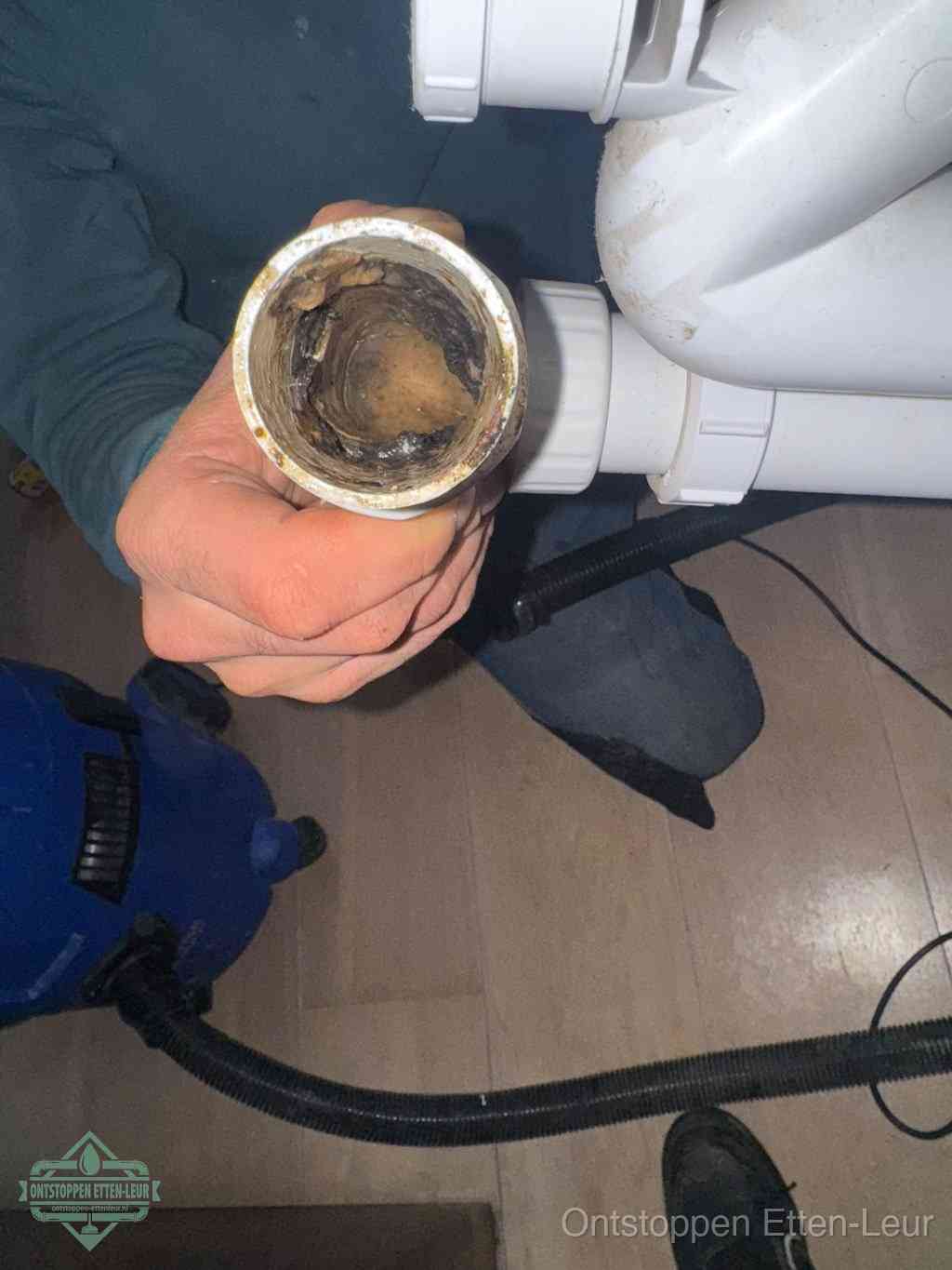 Een hand houdt een losgekoppeld PVC-afvoerbuisstuk vast dat van binnen volledig is dichtgeslibd met vet, vuil en aanslag, de meest voorkomende oorzaak van een verstopte afvoer in Etten-Leur