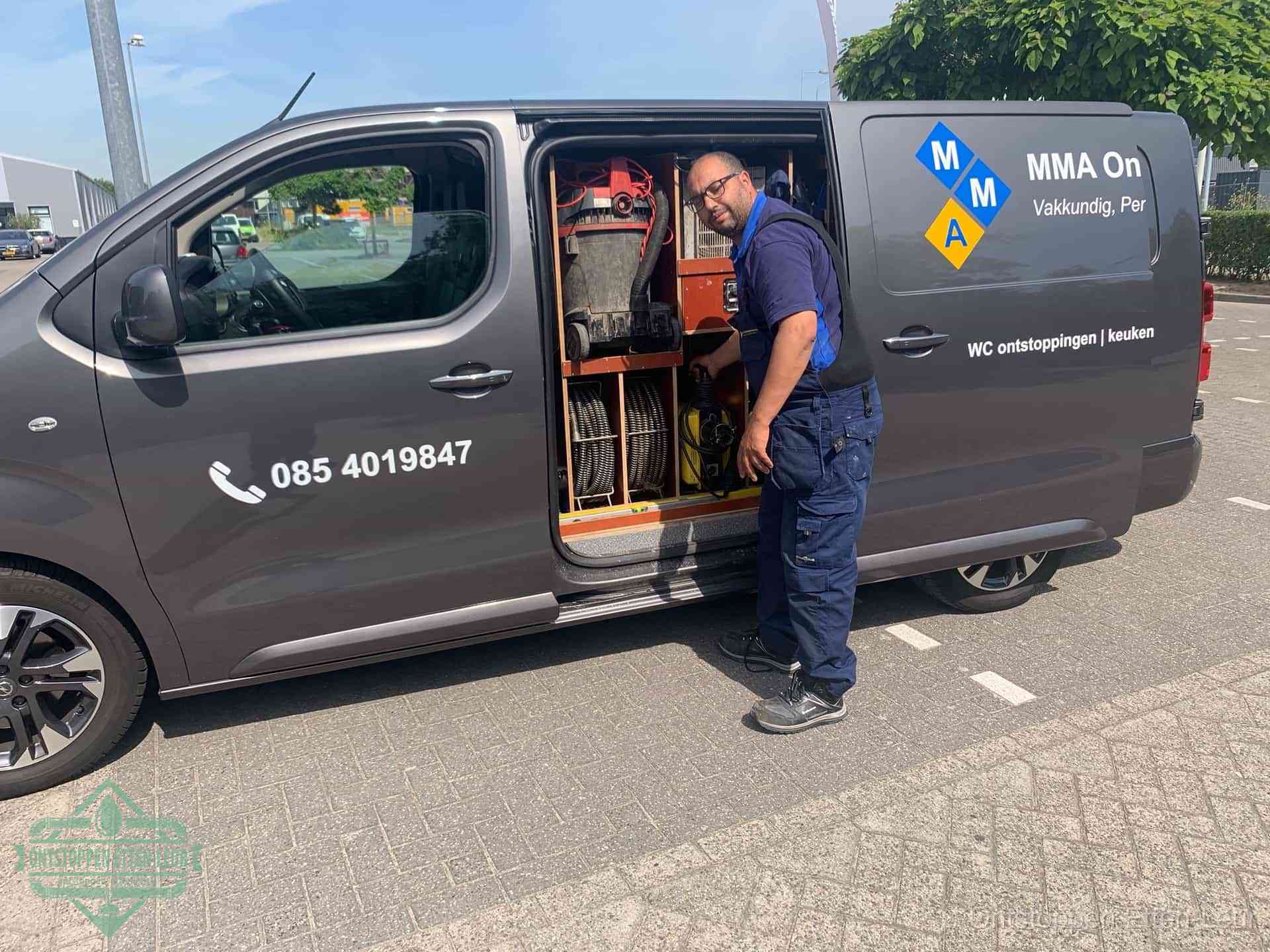 Een monteur bij de open schuifdeur van zijn bedrijfsbus op een parkeerplaats, klaar om de oorzaak van terugkerende afvoerverstoppingen aan te pakken in Etten-Leur