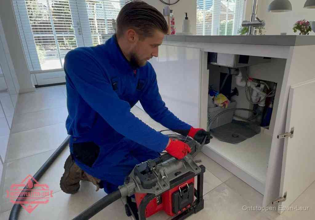 Een monteur voert een professionele elektrische ontstoppingsmachine in de afvoer onder de spoelbak tijdens het gootsteen ontstoppen in Etten-Leur