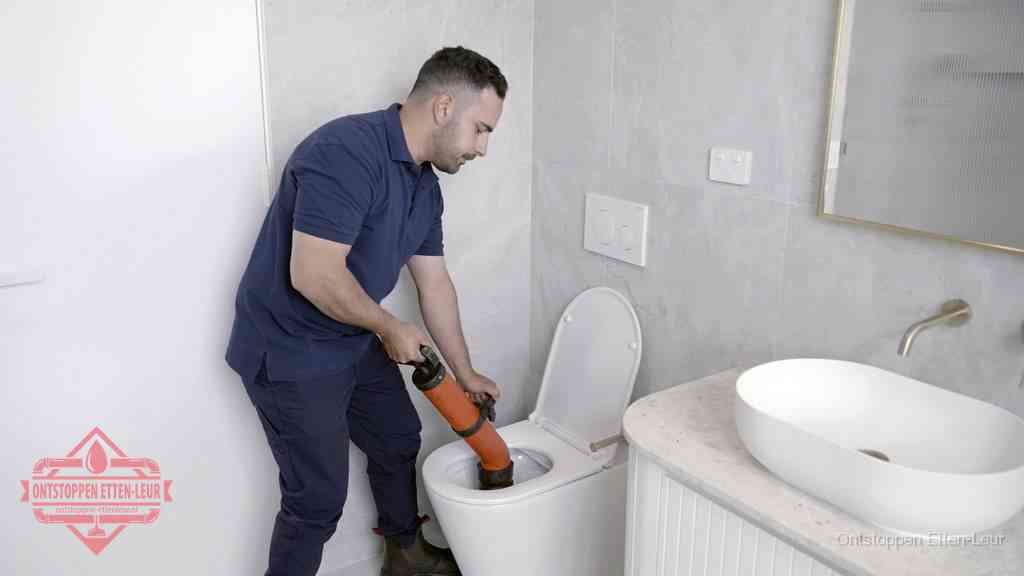Een man gebruikt een handmatige luchtdruk-ontstopper in een modern betegeld toilet om zelf de wc te ontstoppen in Etten-Leur